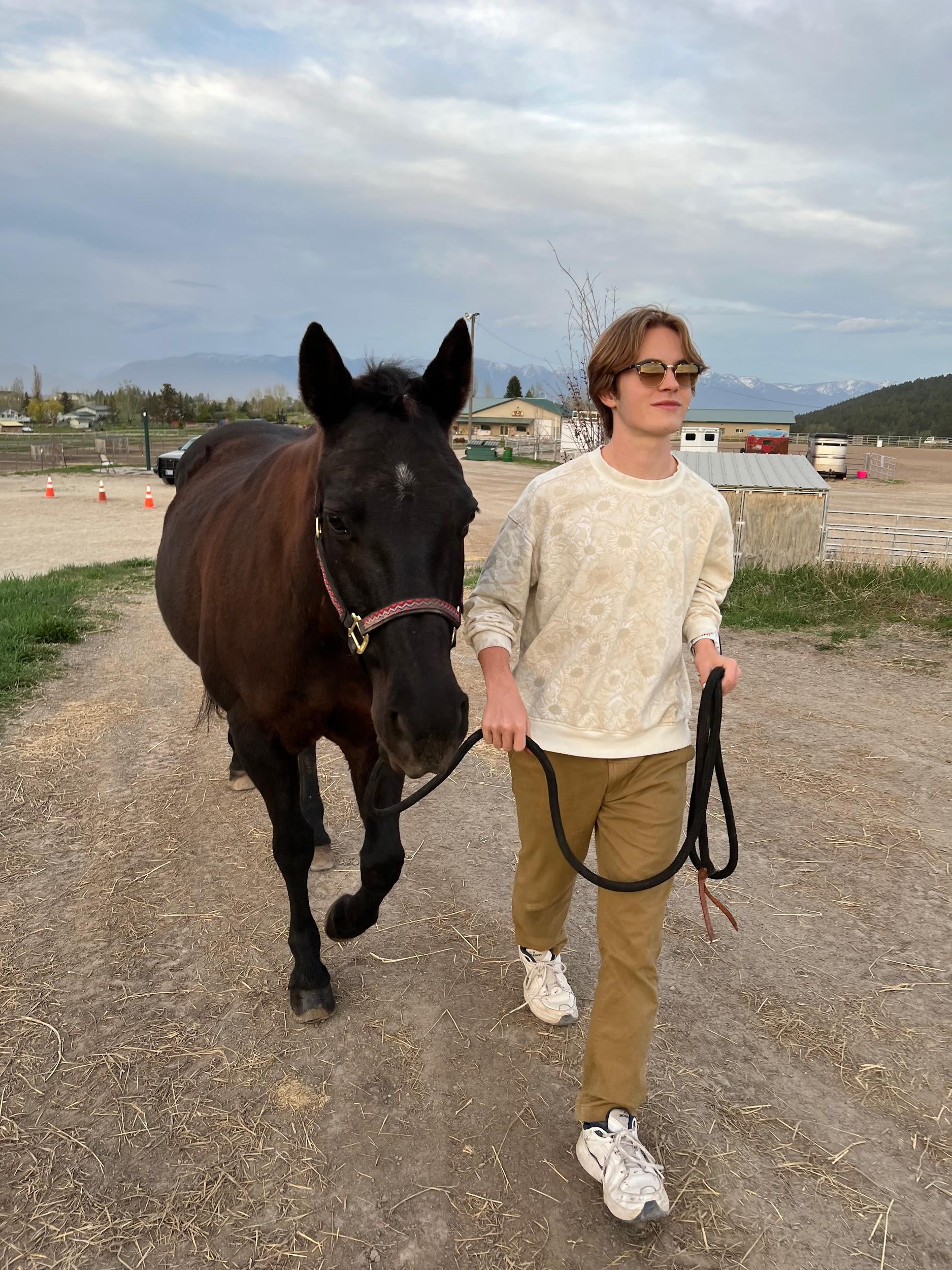 Colton Little walking a horse on a Montana ranch, with the Flathead mountains in the background